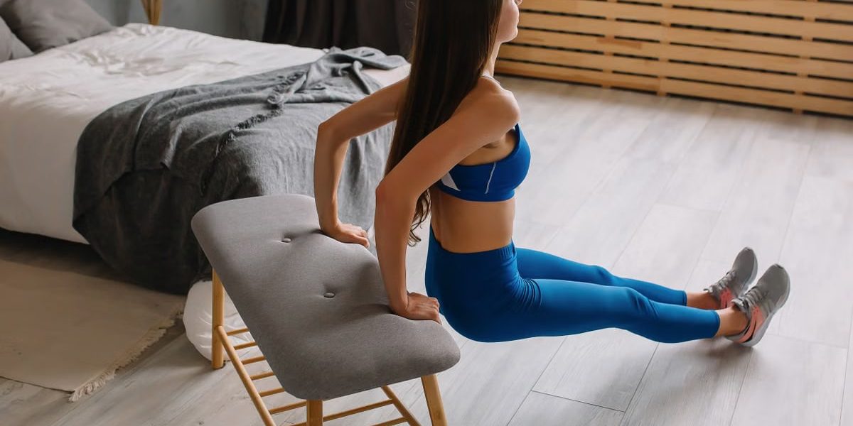 Young woman in sportswear doing tricep dips using bench at home.